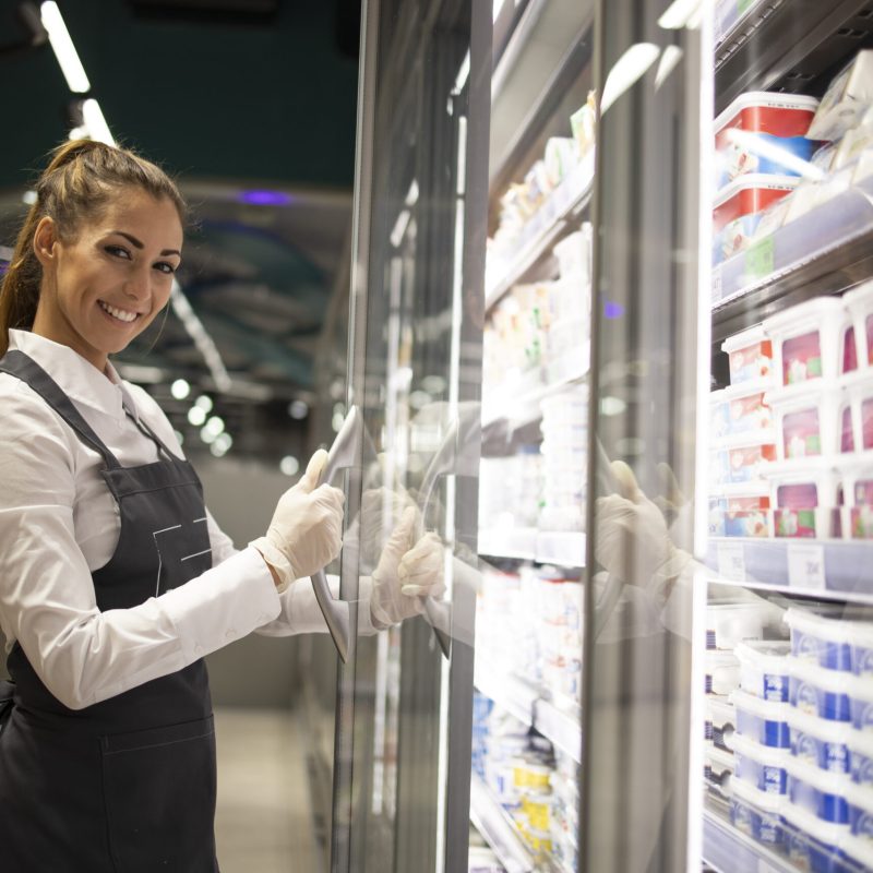 Portrait of supermarket worker standing by the freezer with food.